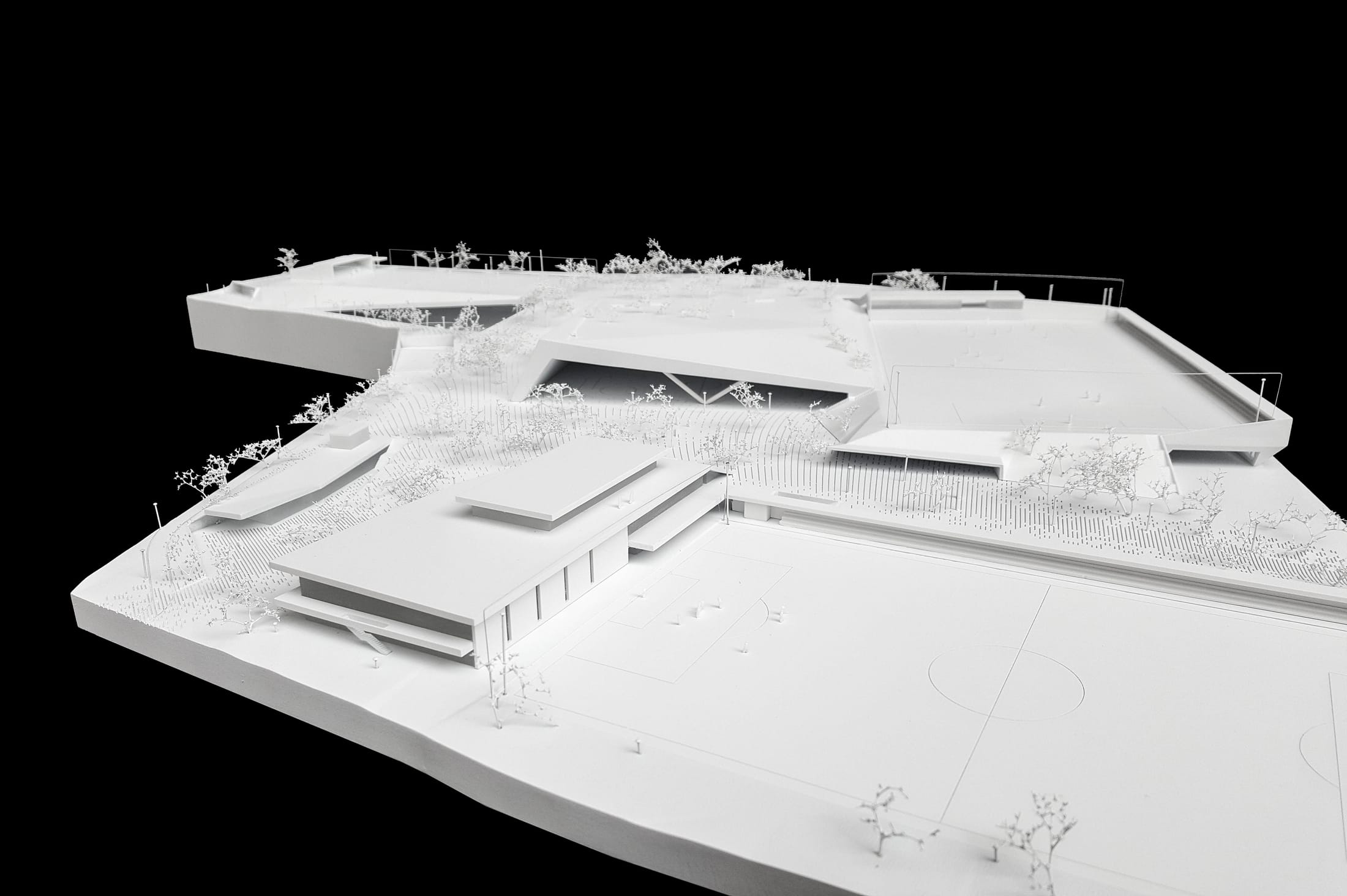 Weißes Architekturmodell einer weitläufigen Sportanlage mit Tribünendach auf schwarzem Grund.